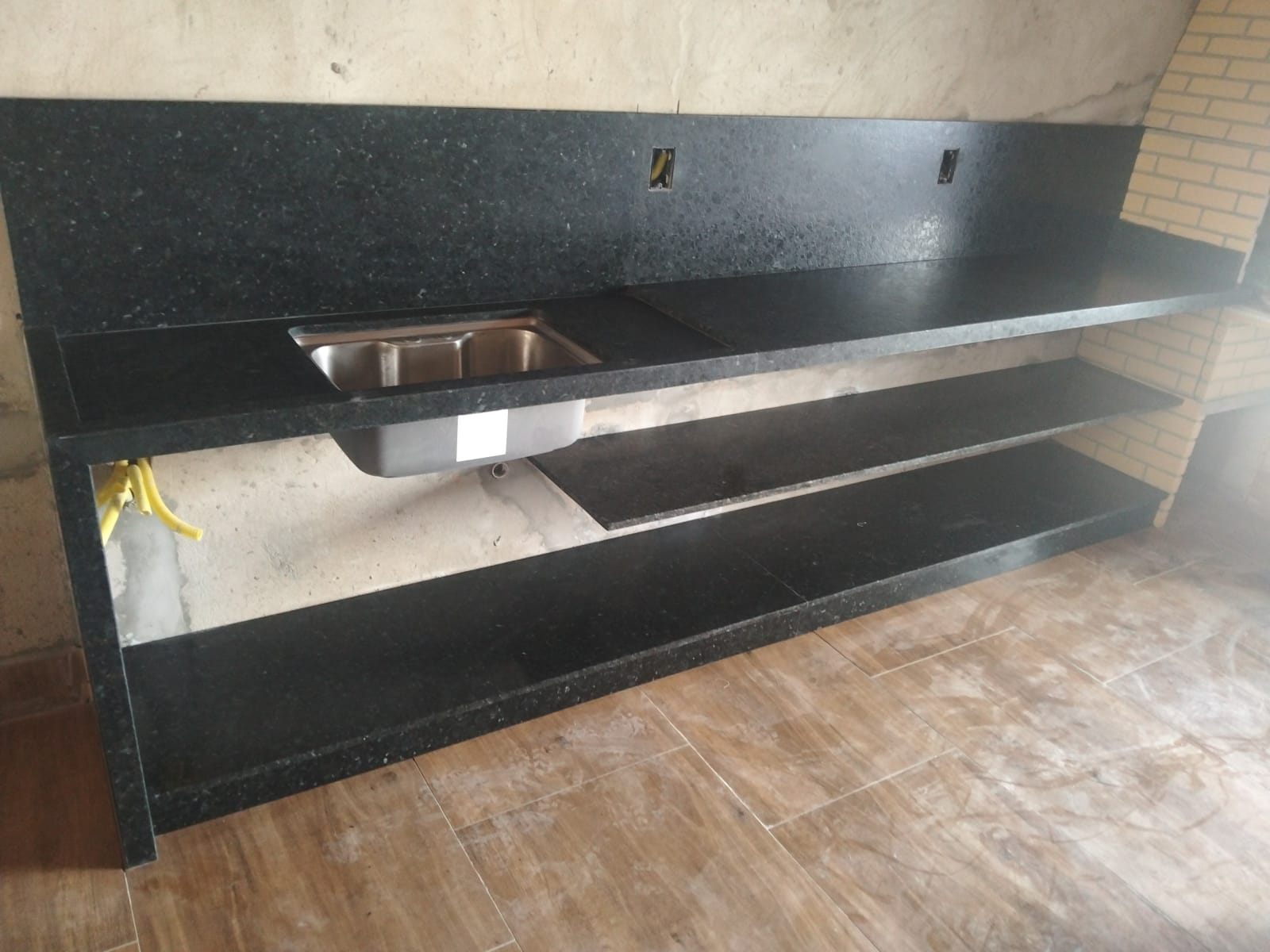 Bancada longa em granito preto com prateleiras e cuba inox